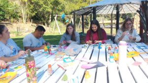 Colaboradores da Rede Cruzada fazendo atividades de corte e colagem, em ambiente aberto.