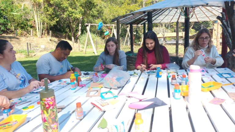 Colaboradores da Rede Cruzada fazendo atividades de corte e colagem, em ambiente aberto.